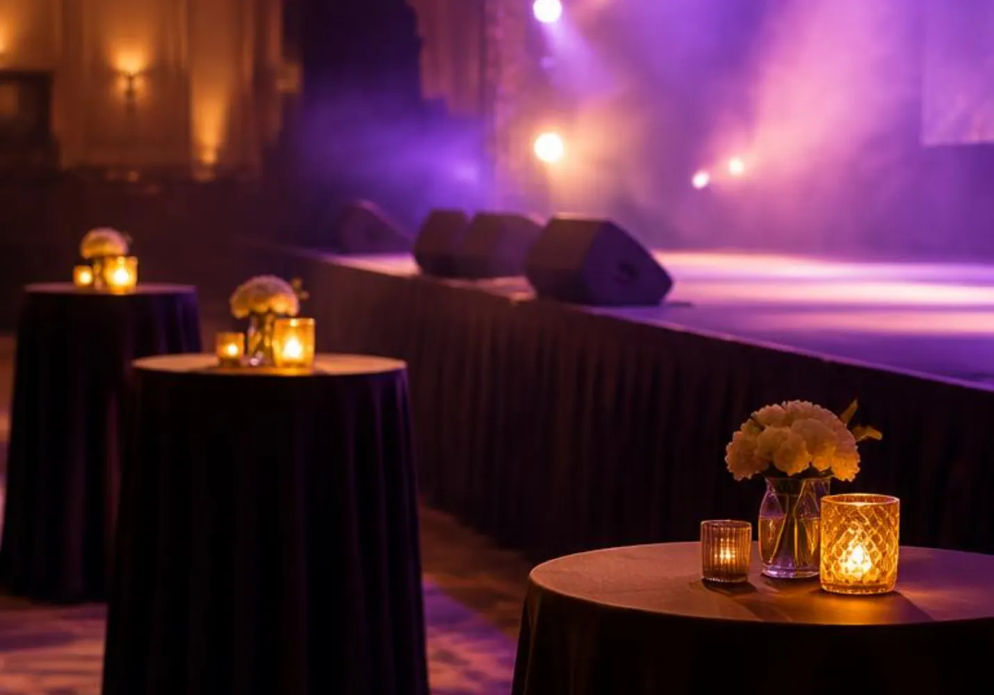 Cocktail tables with candles near a lit stage