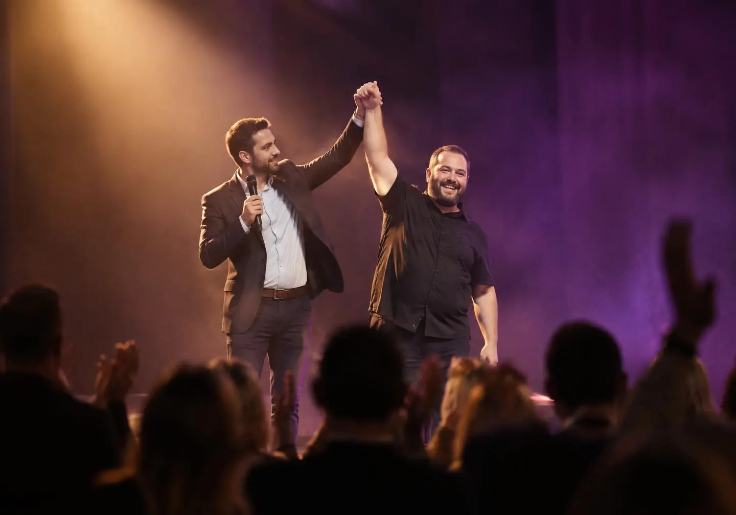 Host raising the winning comedian's arm on stage