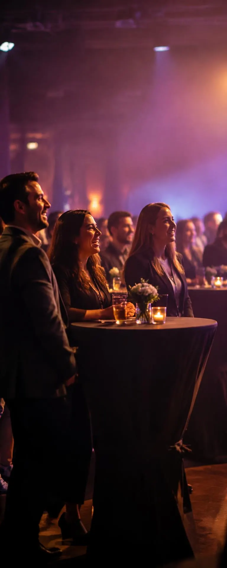 Guests at cocktail tables laughing toward the stage